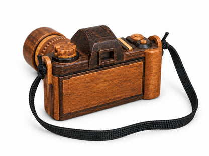 Handmade wooden camera sculpture viewed from the rear, showing its wood body and black strap.
