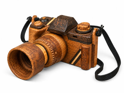 Handmade wooden camera sculpture viewed from the right side, showing its carved lens, wood grain, top controls and black strap against a light background.